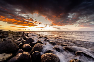 rocks on seashore under gray clouds during sunset