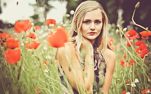 selective landscape photography of woman wearing gray ruffled sleeveless top standing between red petaled rose plants