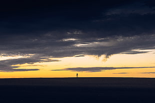 silhouette photo of person standing beneath empty ground under cloudy sky