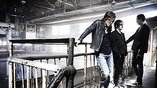 three men band members standing beside brown metal handrails