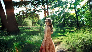 woman wearing orange sleeveless dress standing on pathway surrounded by trees