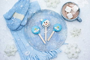cup of chocolate with marshmallow near plate with snowman popsicles