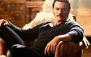 man in black sweater sitting on brown armchair HD wallpaper