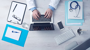 person holding laptop near stethoscope and iphone