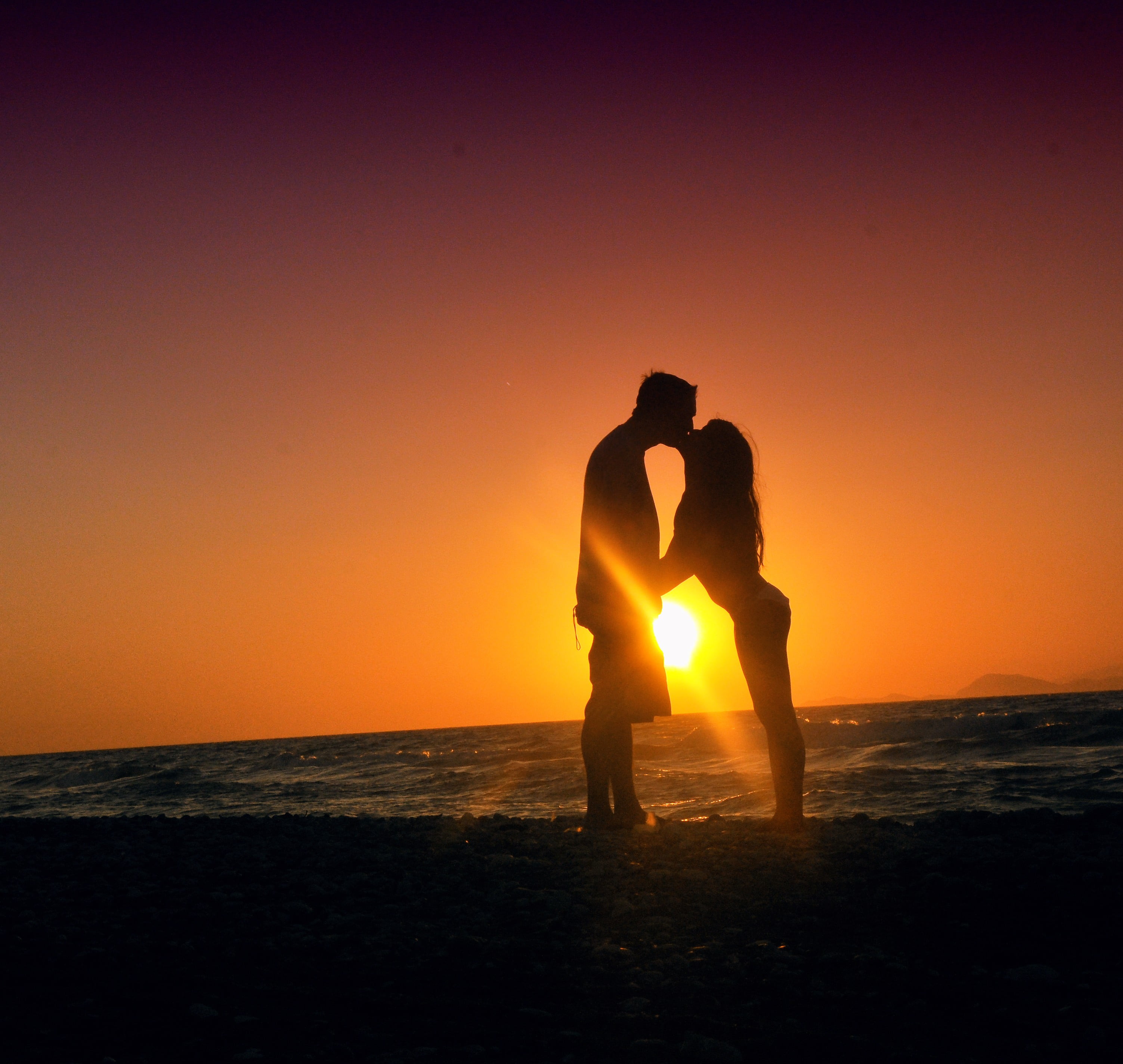 silhouette of man and woman kissing near the seashore during sunset