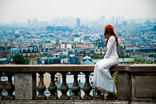women in white dress sitting on building roof fence