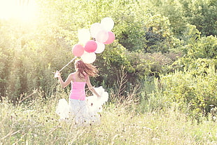 women in pink tank top carrying pink and white cluster balloons