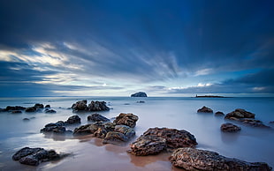 time lapse photography of rocks on seashore under cloudy sky