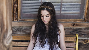 woman in white sleeveless dress sitting looking down with brown headband