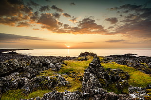 gray rocks and green grass ground near body of water under white cloudy sky during sunset