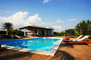 rectangular swimming pool near white concrete house under blue and white sky at daytime