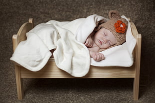 baby in brown knit critter cap laying on brown bed