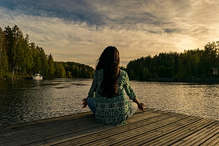 woman on green dress shirt sitting on brown wooden dock beside swamp