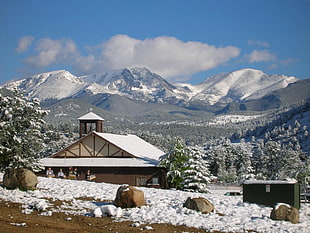 snow-covered brown cabin with snow-capped mountains in the background