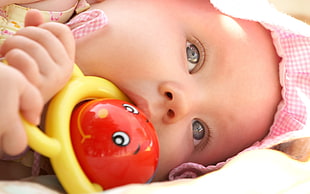 baby holding yellow and red plastic toy