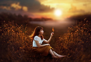 woman in white shirt and brown skirt sitting near grasses