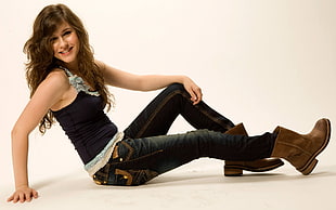 woman wearing black spaghetti strap shirt and black denim jeans outfit with brown leather boots sitting on white floor
