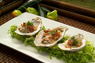 three oysters with green leafy vegetables on ceramic bowl