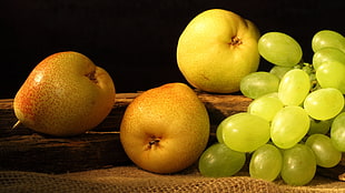 green grapes and yellow apple fruits on brown wooden surface