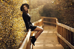 woman in black long-sleeved mini dress sits on brown wooden pathway rail overlooking sunset