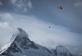 red helicopter hovering above snow-filled mountain