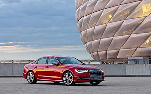 photography of red Audi sedan beside gray building during daytime