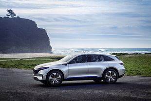 silver sports utility vehicle concept on grey concrete road near green grass field in distant of body of water and mountain